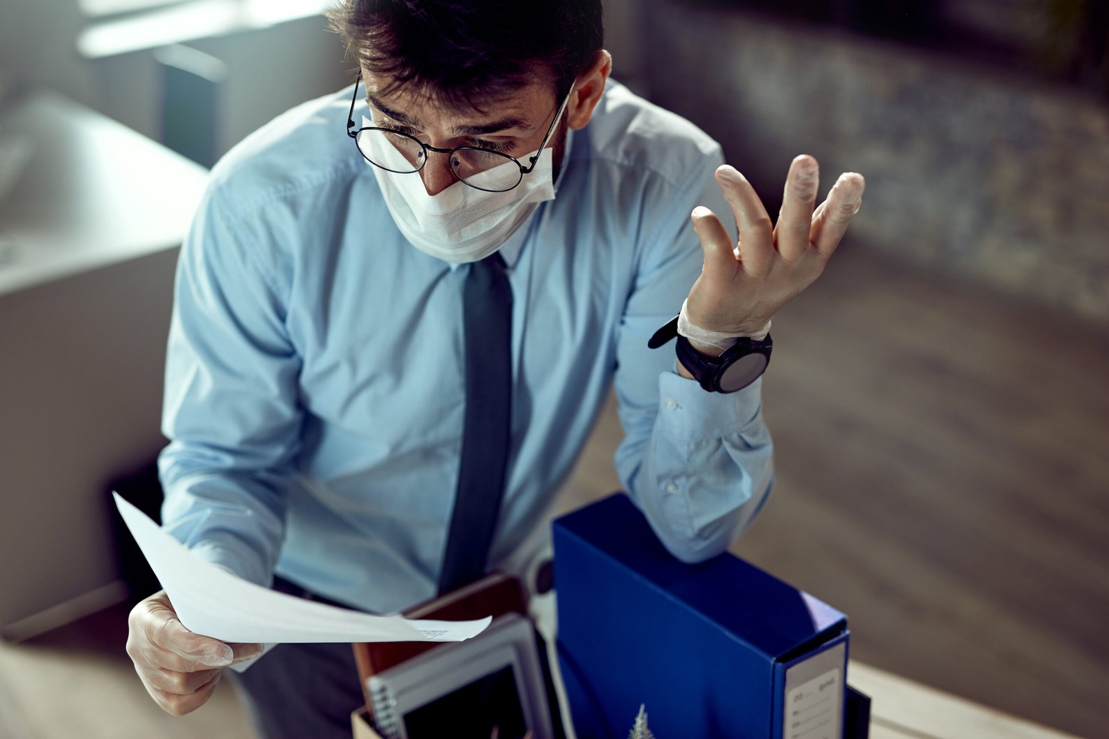Fired businessman wearing face mask and feeling frustrated while reading a notice in the office.