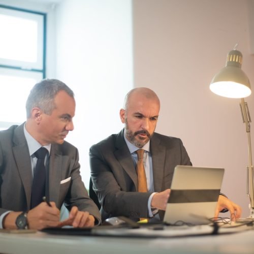 Portrait of successful businessmen in office. Two serious man in suits working with computer at table, making decisions and developing strategy for business growth. Business growth and finance concept